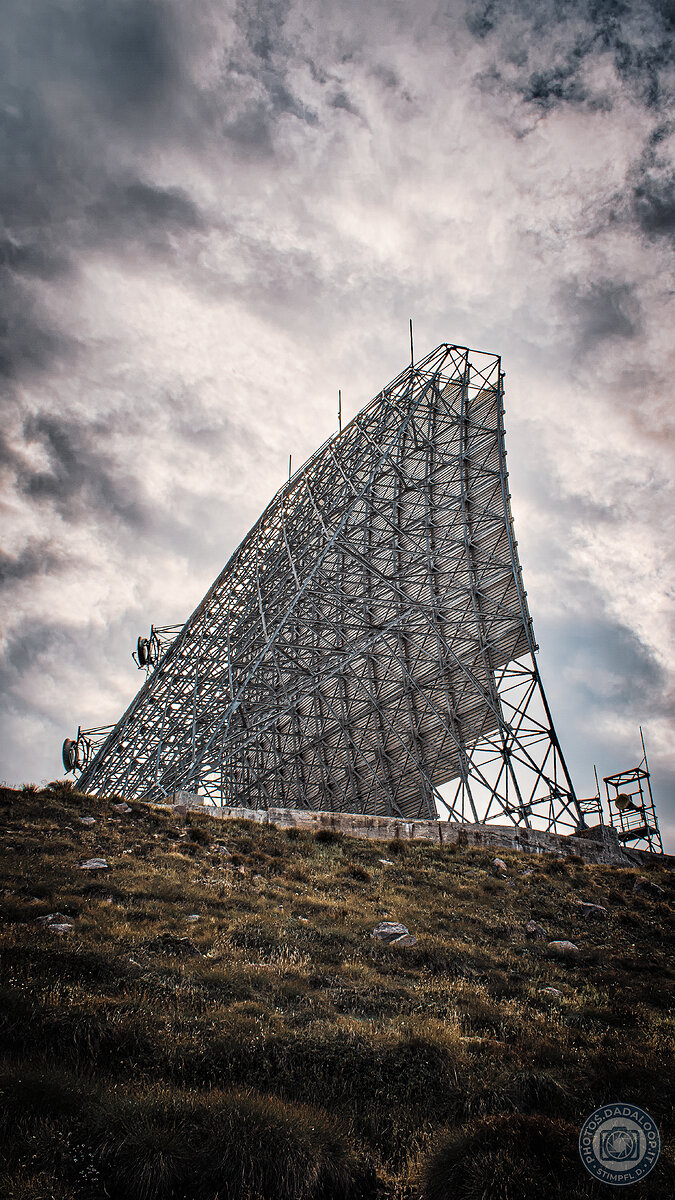 Antenna parabolica gigante su collina erbosa sotto cielo nuvoloso