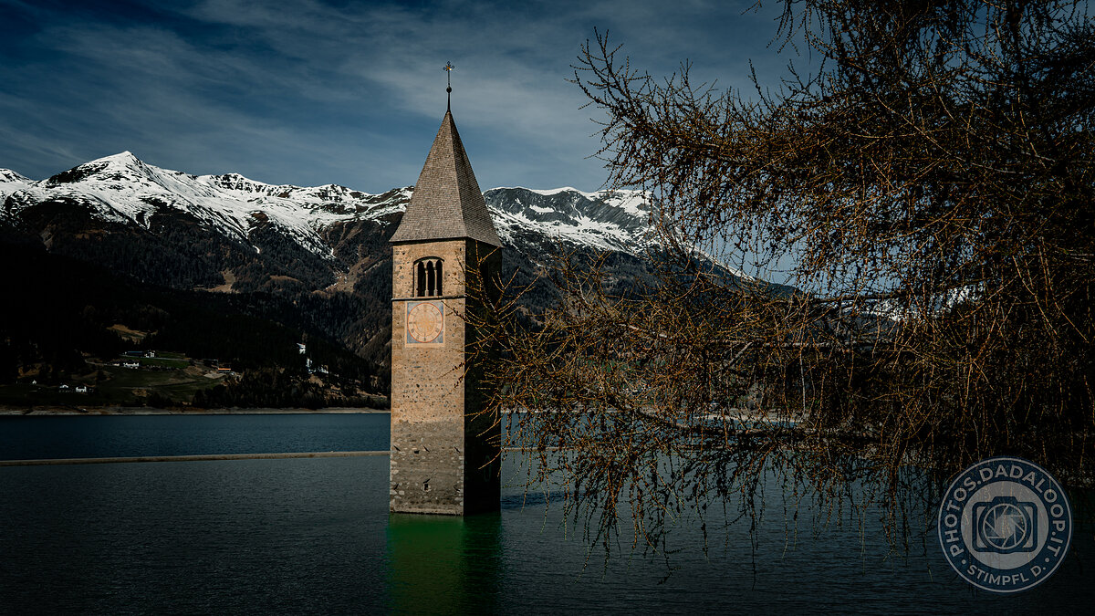 Campanile sommerso nel lago di Resia con montagne innevate e cielo cupo