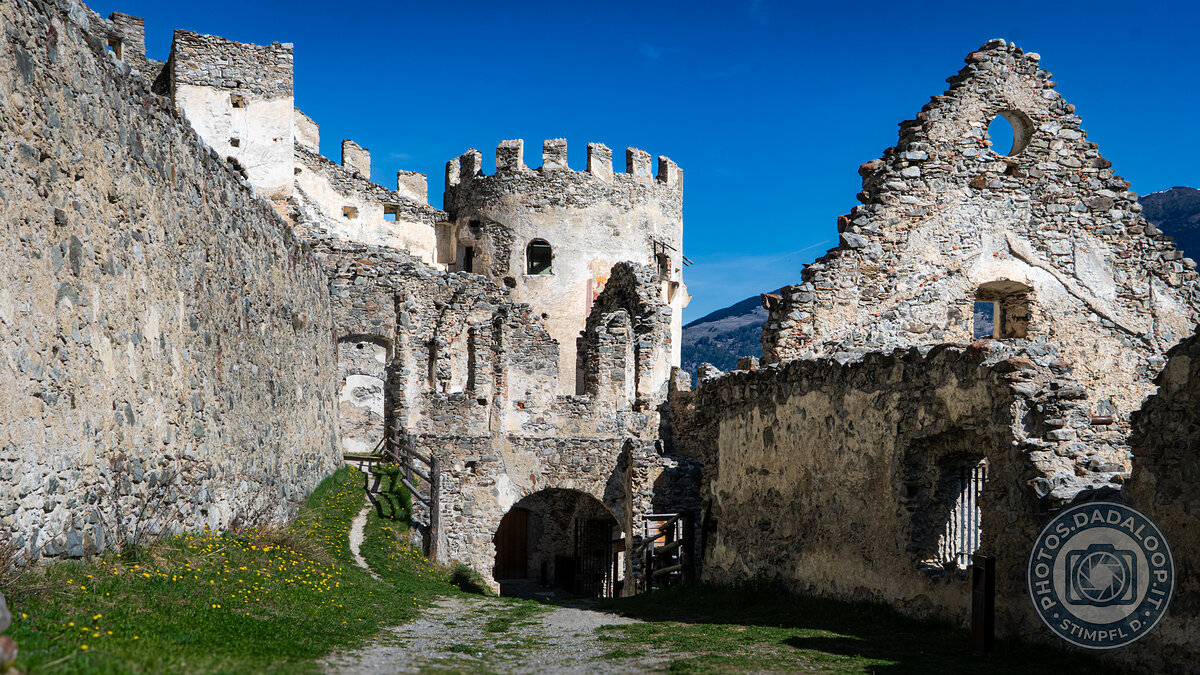 Ruins of an ancient stone castle under a clear blue sky, with mountains in the background