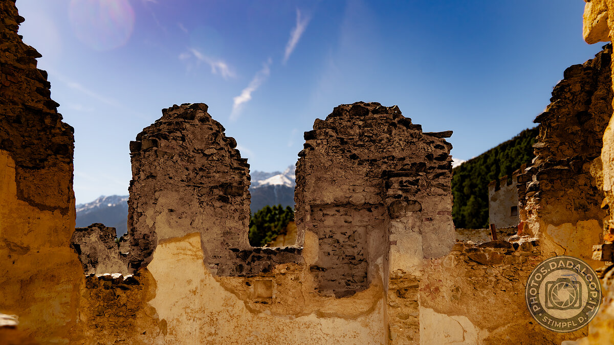 Rovine di un castello con vista sulle Alpi innevate sotto un cielo azzurro