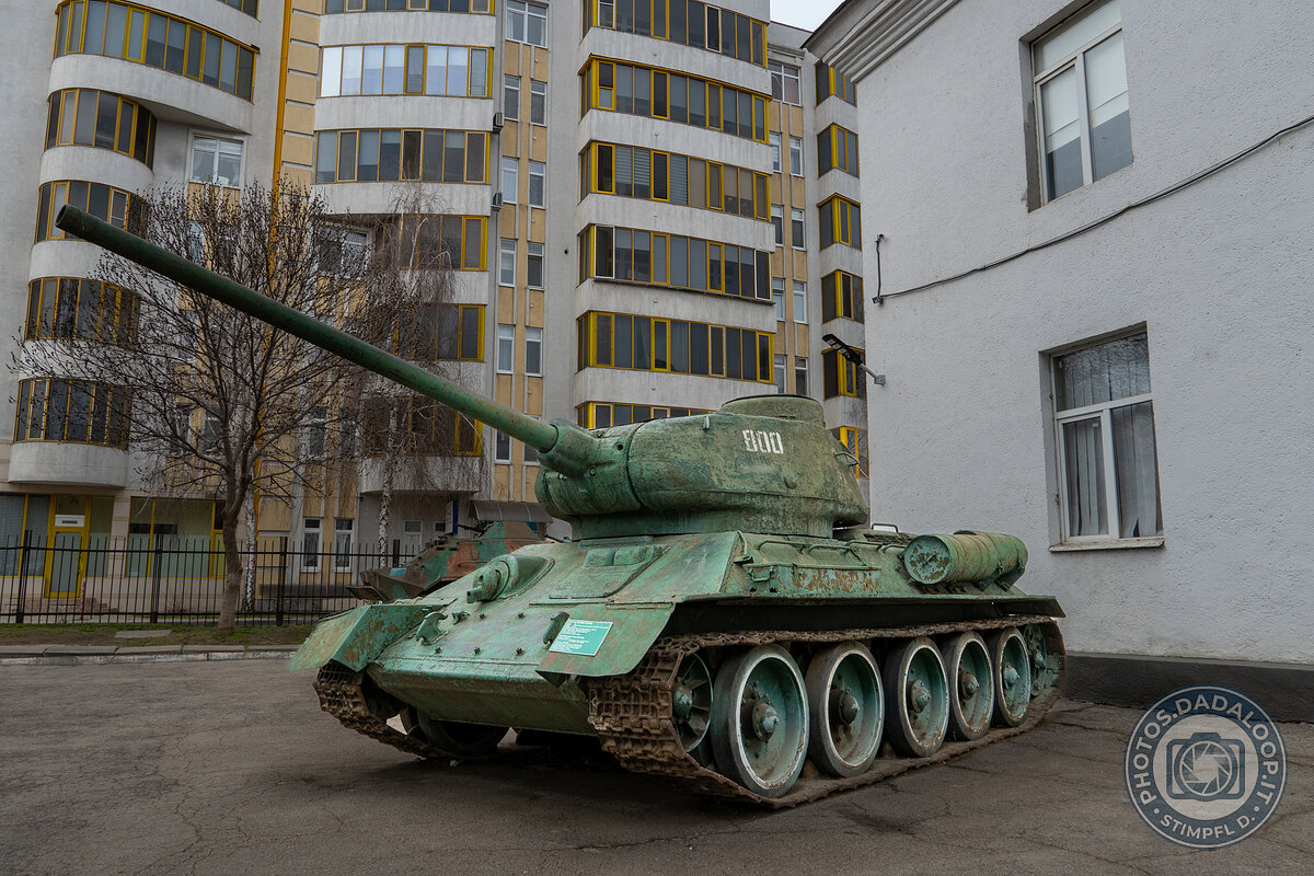 Rusty T-34 tank in front of a residential building