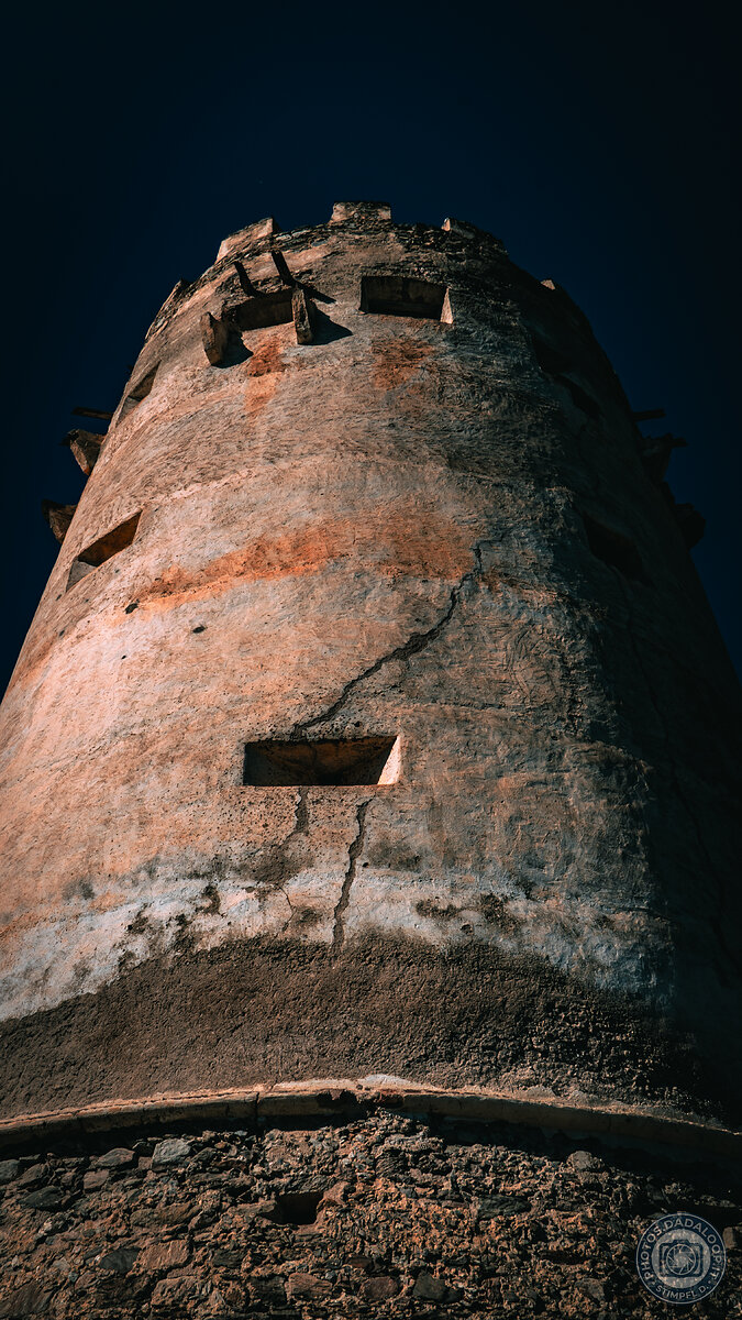 Antica torre in pietra con crepe sotto un cielo drammatico e scuro