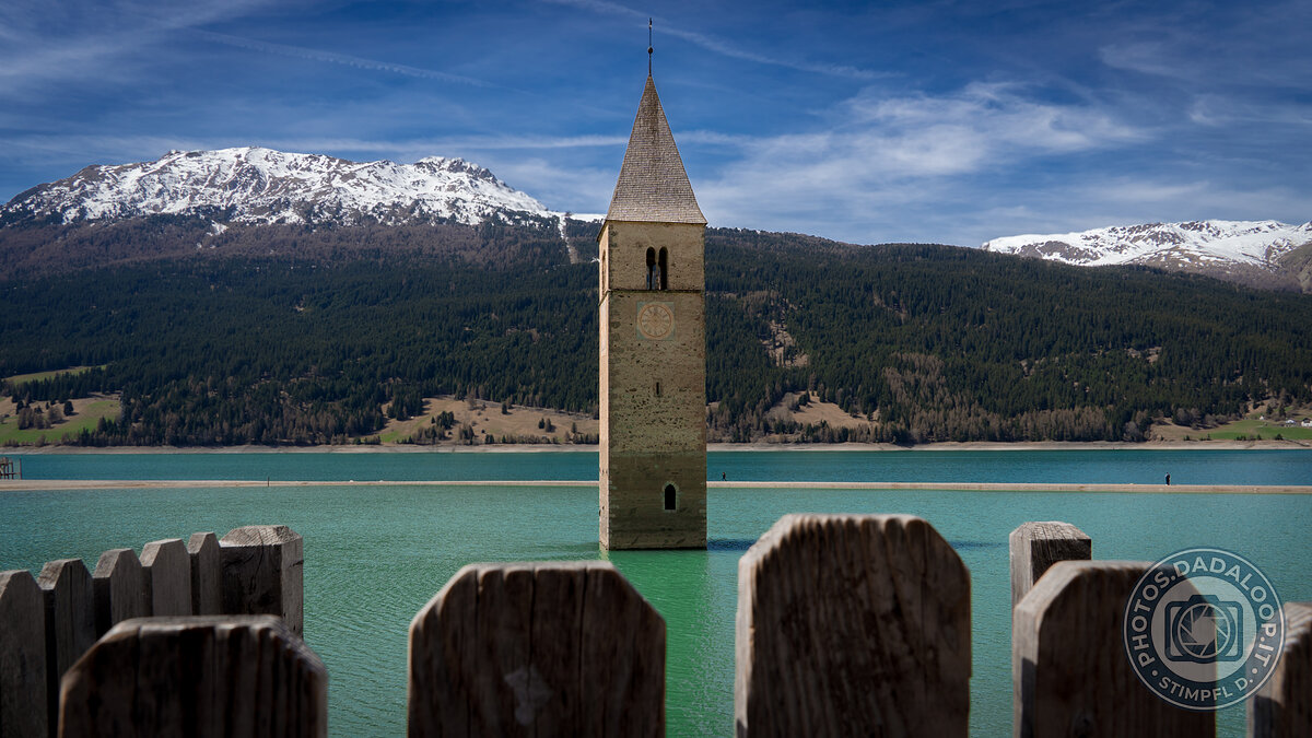 Iconico campanile sommerso nel Lago di Resia con montagne innevate e cielo blu