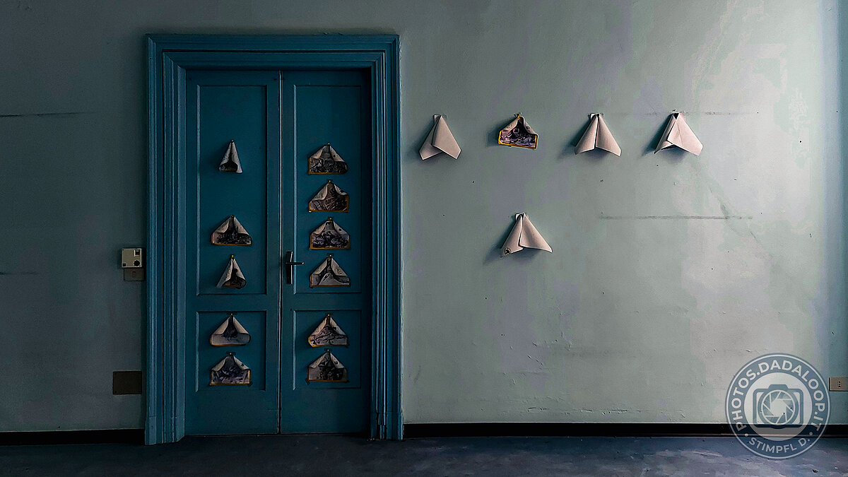 Installazione artistica con barchette di carta su porta e parete azzurra