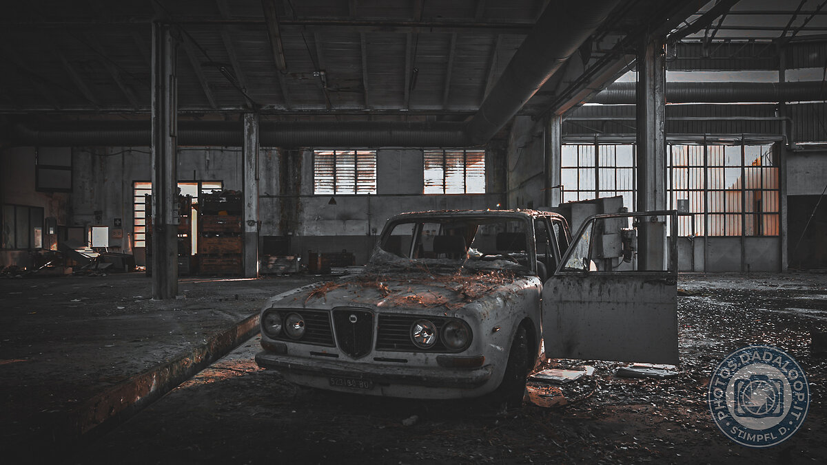 Vecchia auto d'epoca abbandonata in una fabbrica in rovina, illuminata dal sole