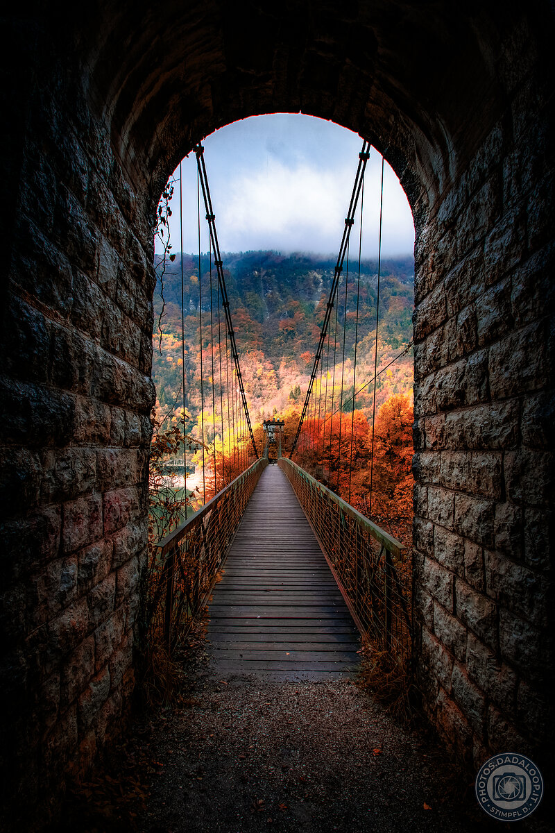 Ponte sospeso incorniciato dall'arco di pietra, colori autunnali